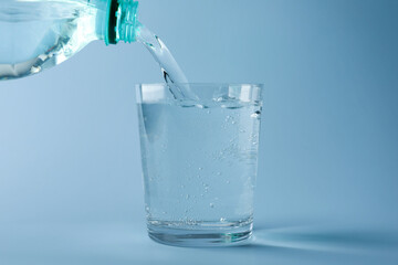 Pouring refreshing soda water from bottle into glass on light blue gradient background, closeup