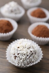 Delicious homemade candies with cocoa powder and coconut flakes on wooden table, closeup