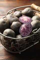 Raw purple potatoes in metal basket on wooden table, closeup