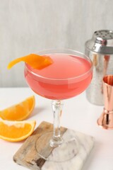Martini cocktail with garnish, slices of orange and bartender equipment on white table, closeup