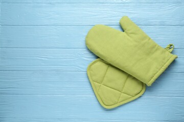 Green oven glove and potholder on light blue wooden table, flat lay. Space for text