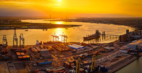 Golden hour drone shot of the busy Port of London, highlighting industrial activity, cranes, and shipping containers by the River Thames. Perfect for logistics, trade, and infrastructure visuals