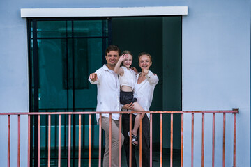 A happy family of three shares a loving moment on the balcony of their modern home. The daughter...