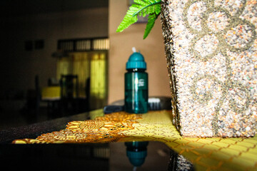 Indoor shot with focus on a green water bottle and decorative stone vase on a patterned table, with...