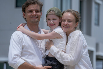 A hopeful young family looks towards their future outside a new modern home. The father holds their daughter, who points excitedly, as the mother smiles, dreaming of their life together.