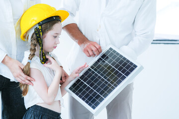 A curious young girl in a yellow hard hat learns about renewable energy. An adult teaches her about a solar panel, sparking interest in sustainability and future green technology.