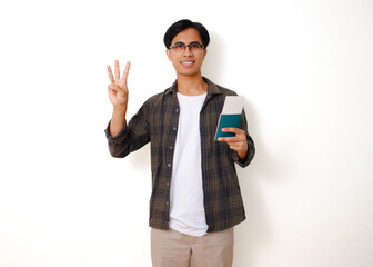 Smiling Asian tourist man holding a passport and boarding pass, showing a three-finger gesture, isolated on a white background