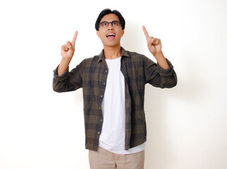 Excited young Asian man pointing and looking upwards with a happy expression, isolated on white...