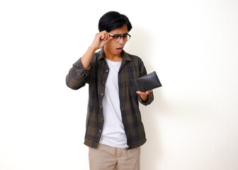 Sad young Asian man holding and showing an empty wallet with a stressed expression, isolated on a white background