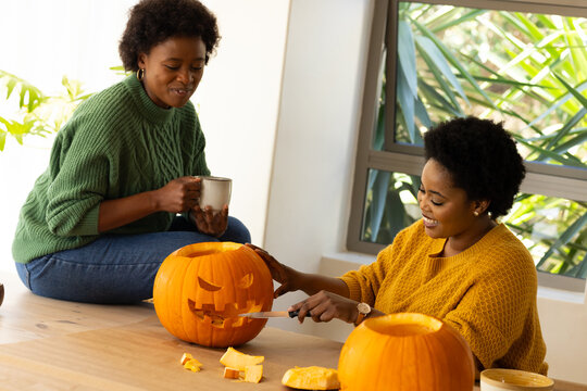Halloween time, Carving pumpkins, african american female friends enjoying coffee together at home