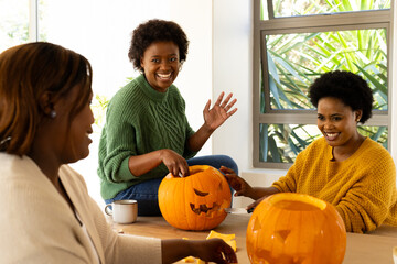 Halloween time, african american female friends carving pumpkins at home