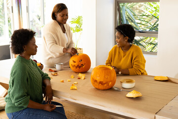 Halloween time, african american female friends carving pumpkins together at home