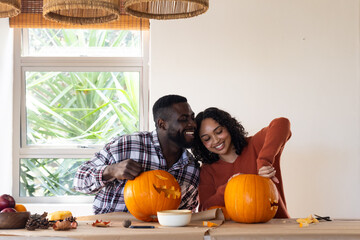 Halloween time, multiracial couple carving pumpkins together at home