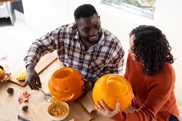 Halloween time, smiling multiracial couple carving pumpkins together at home