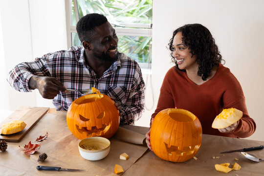 Halloween time, smiling multiracial couple carving pumpkins at home - Powered by Adobe