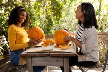 Halloween time, carving pumpkins on deck, multiracial female friends preparing together