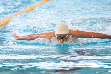 Swimmer boy swims butterfly swimming style in the pool