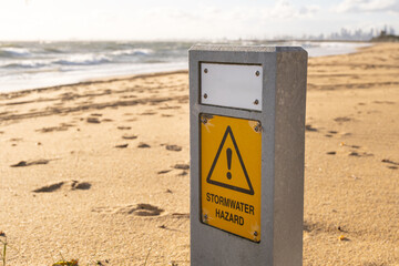 Stormwater hazard warning sign on a sandy beach at Brighton, suburban Melbourne, Australia. A...