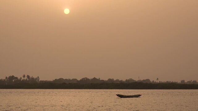 SENEGAL - 7.31.2025 - An empty pirogue rests in the water off the coast of Senegal at sunset.