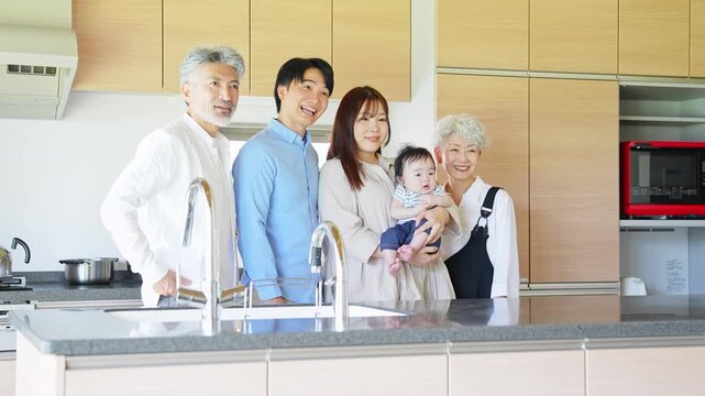 A smiling three-generation family surrounding a baby in a house