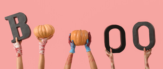 Hands of zombies with word BOO and ripe pumpkins on pink background. Halloween celebration