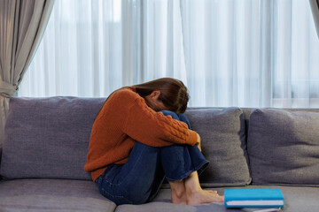 Asian woman feeling stress and headache on sofa. She used her hand to touch her face she has a...