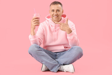 Mature man pointing at glass of fruit smoothie on pink background
