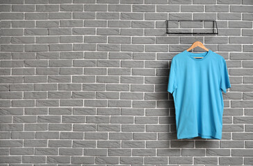 Stylish blue t-shirt hanging on grey brick wall