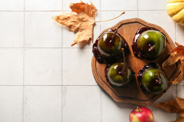 Tasty caramel apples for Halloween and autumn leaves on white tile background
