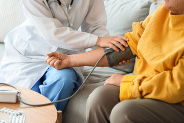 Doctor measuring blood pressure of senior woman at home, closeup