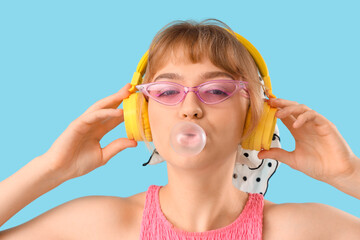 Beautiful young woman in headphones with chewing gum on blue background, closeup