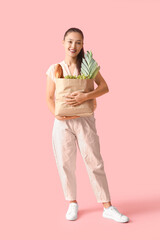 Young Asian woman with shopping bag full of fresh food on pink background