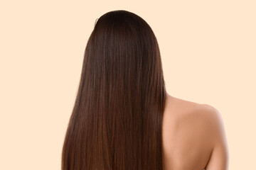 Young brunette woman with beautiful hair on beige background, back view