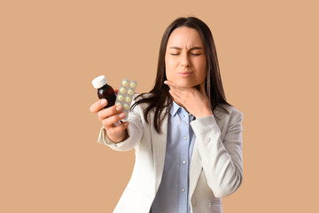 Young woman with syrup and pills for sore throat on brown background