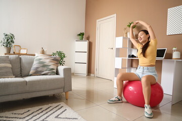 Young Asian woman stretching on fitball at home