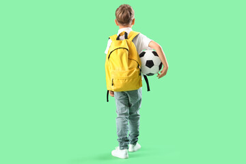 Little schoolboy with backpack and soccer ball on green background, back view