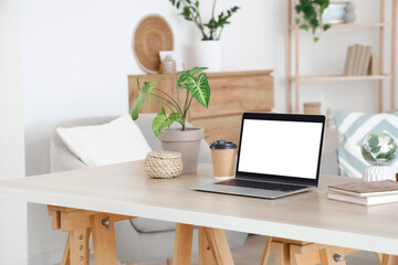 Blank laptop with coffee cup and plants on programmer's desk in living room