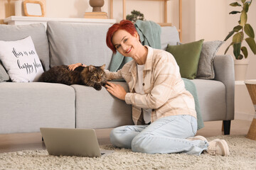 Beautiful happy mature woman with cute cat and laptop sitting at home