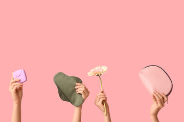 Many female hands with reusable pad, tampons storage box and cosmetic bag on pink background