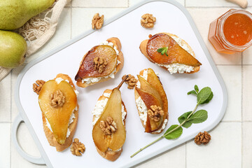 Tray of pear bruschetta with ricotta cheese, walnuts and jar of honey on white tile background