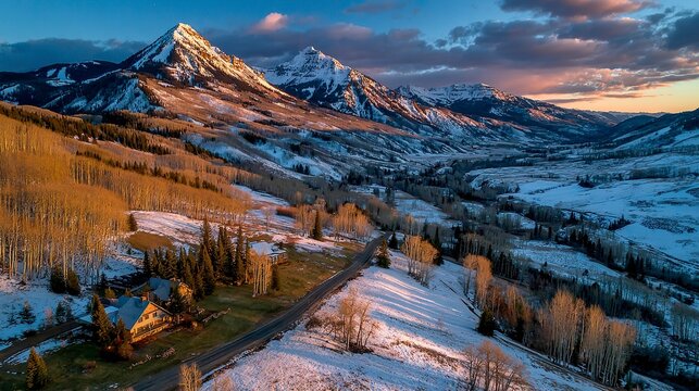 Panoramic aerial view of rugged snowy mountains at sunset, with golden light casting long shadows on the slopes  