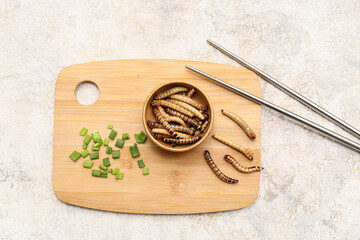Wooden bowl with fried maggots and green onion on white background