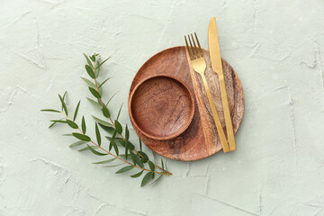 Stylish table setting with wooden plate, bowl, cutlery and plant branches on green grunge background