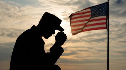 Silhouette of a soldier praying before the american flag at sunset