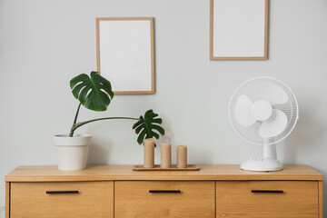 Electric fan with candles and palm plant on chest of drawers in room