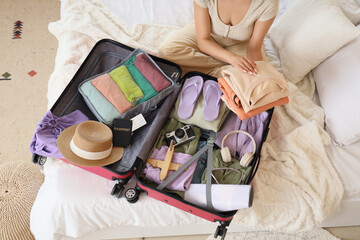 Young woman packing clothes into suitcase for trip in bedroom, top view