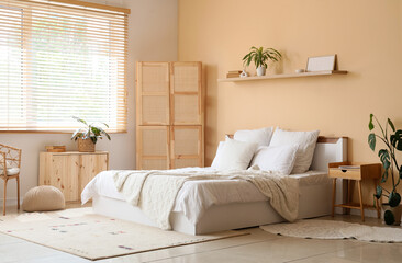 Interior of cozy bedroom with wooden folding screen, shelf and plants