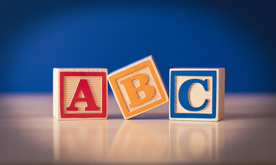 Wooden ABC blocks with red, orange, and blue letters on reflective surface