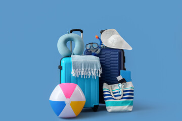 Suitcases, inflatable ball and beach accessories on blue background