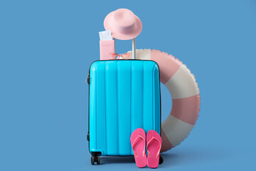 Suitcase, inflatable ring and beach accessories on blue background